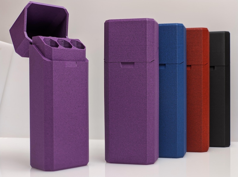 Puede incluir: Una colecci&oacute;n de estuches rectangulares en varios colores: morado, azul, rojo y negro. El estuche morado est&aacute; abierto, revelando tres compartimentos cil&iacute;ndricos. Los estuches tienen una superficie texturizada y un dise&ntilde;o geom&eacute;trico.