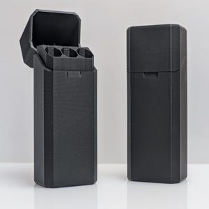 Puede incluir: Dos estuches rectangulares negros, uno abierto y otro cerrado. El estuche abierto revela compartimentos interiores. Los estuches tienen un acabado mate y un dise&ntilde;o geom&eacute;trico. Los estuches probablemente son para guardar objetos peque&ntilde;os.