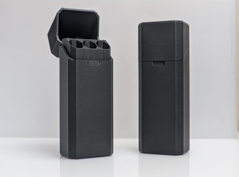 Puede incluir: Dos estuches rectangulares negros, uno abierto y otro cerrado. El estuche abierto revela compartimentos interiores. Los estuches tienen un acabado mate y un dise&ntilde;o geom&eacute;trico. Los estuches probablemente son para guardar objetos peque&ntilde;os.