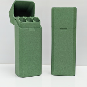Puede incluir: Dos estuches rectangulares verdes, uno abierto y otro cerrado, se muestran sobre un fondo blanco. El estuche abierto revela tres compartimentos cil&iacute;ndricos. Los estuches tienen una superficie texturizada y una tapa con bisagras. El estuche cerrado tiene una peque&ntilde;a hendidura en la tapa.