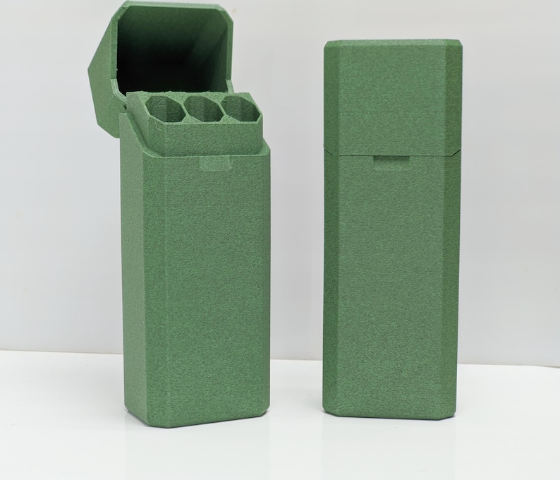 Puede incluir: Dos estuches rectangulares verdes, uno abierto y otro cerrado, se muestran sobre un fondo blanco. El estuche abierto revela tres compartimentos cil&iacute;ndricos. Los estuches tienen una superficie texturizada y una tapa con bisagras. El estuche cerrado tiene una peque&ntilde;a hendidura en la tapa.