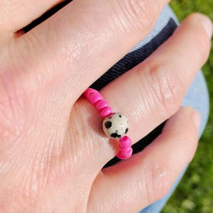 Könnte beinhalten: Ein rosafarbener Perlenring mit einer einzigen weißen und schwarzen, gefleckten Steinperle.