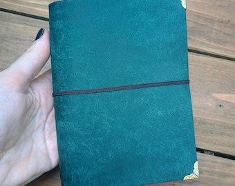 Cuaderno de viaje de piel color turquesa tamaño A6 con esquinas metálicas.