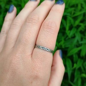 May include: A silver ring with a delicate floral design. The ring is worn on a finger with blue nail polish.