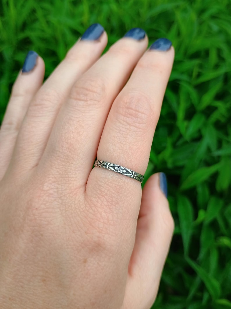 May include: A silver ring with a delicate floral design. The ring is worn on a finger with blue nail polish.