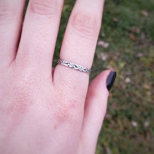 May include: A silver ring with a delicate floral design. The ring is worn on the ring finger of a hand.