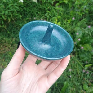 Puede incluir: Un plato de cer&aacute;mica redondo con un cono central para guardar joyas, que presenta un esmalte azul verdoso profundo satinado con una textura sutilmente moteada. El texto SATINY DEEP TEAL aparece impreso en la parte superior de la imagen.