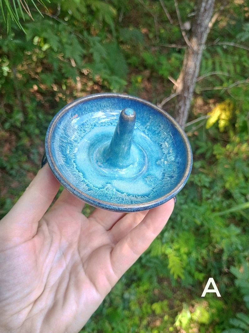 Puede incluir: Un soporte de cer&aacute;mica circular para anillos con un cono central para guardar joyas. La pieza tiene un esmalte brillante con un degradado de azul marino profundo en el borde exterior que transiciona a un azul turquesa vibrante en el centro.