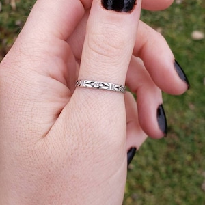 May include: A silver ring with a floral design on the thumb of a hand with black nail polish.