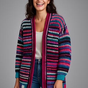 May include: A colorful, striped cardigan in shades of pink, purple, teal, and black. The open-front sweater has a ribbed texture and long sleeves. The trim is a solid magenta color. The model is wearing blue jeans and a white top.