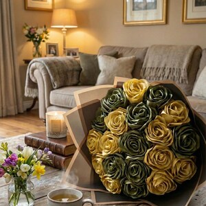 Handmade forever flower bouquet featuring olive green and golden yellow satin ribbon roses wrapped in elegant translucent brown paper. A luxury long lasting floral gift designed for weddings, anniversaries, Mother’s Day, and romantic occasions. Displayed in a modern neutral interior setting with jewelry box and soft natural light. A timeless artificial rose bouquet that never fades and serves as a keepsake floral arrangement.