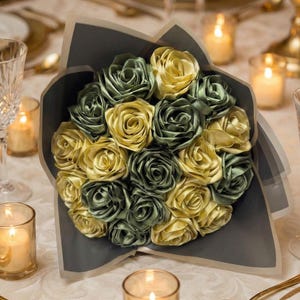 Handmade forever flower bouquet featuring olive green and golden yellow satin ribbon roses wrapped in elegant translucent brown paper. A luxury long lasting floral gift designed for weddings, anniversaries, Mother’s Day, and romantic occasions. Displayed in a modern neutral interior setting with jewelry box and soft natural light. A timeless artificial rose bouquet that never fades and serves as a keepsake floral arrangement.