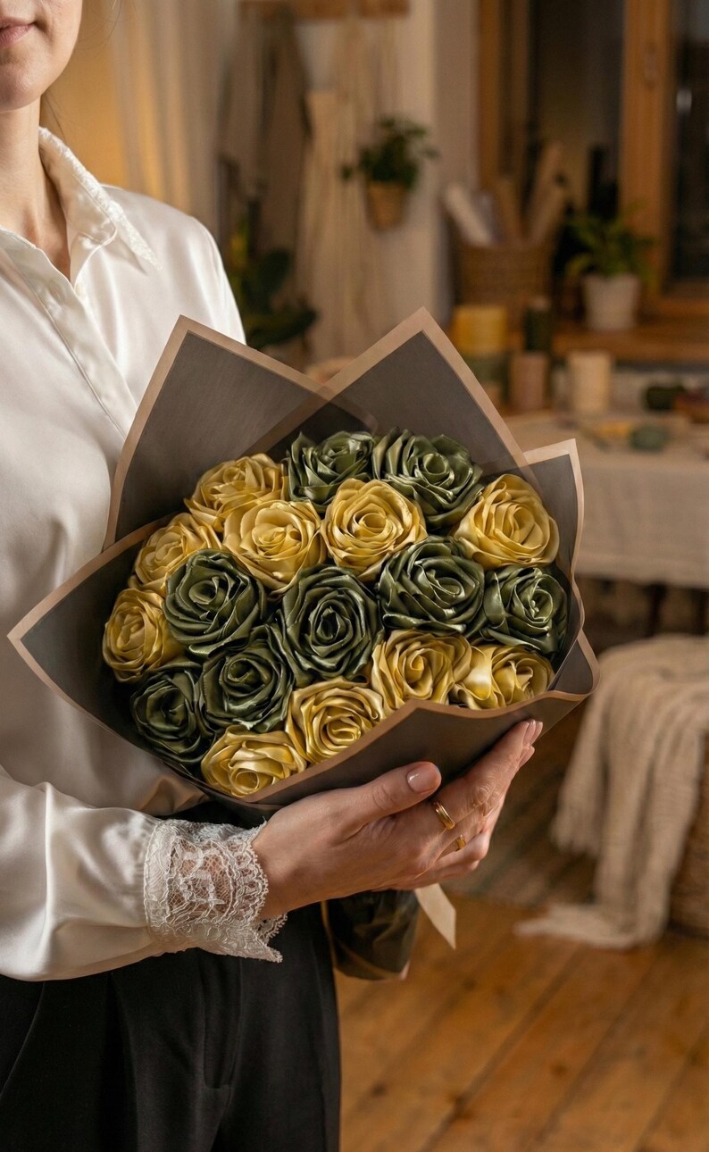 Handmade forever flower bouquet featuring olive green and golden yellow satin ribbon roses wrapped in elegant translucent brown paper. A luxury long lasting floral gift designed for weddings, anniversaries, Mother’s Day, and romantic occasions. Displayed in a modern neutral interior setting with jewelry box and soft natural light. A timeless artificial rose bouquet that never fades and serves as a keepsake floral arrangement.