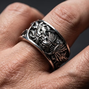 Puede incluir: Un anillo plateado con un diseño detallado de dragón. El anillo presenta un intrincado relieve de un dragón que se envuelve alrededor de la banda. Las escamas y los rasgos del dragón están claramente definidos.
