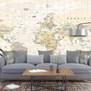 Puede incluir: Un salón con un papel pintado de mapa del mundo. Un sofá gris con cojines se encuentra frente al mapa. Una mesa de centro de madera, una lámpara de pie y una planta en maceta completan la decoración.