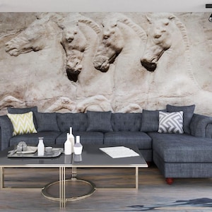 May include: A modern living room featuring a gray sectional sofa with decorative pillows and a rectangular coffee table. The wall behind the sofa displays a large, textured mural of four white horses. The room is illuminated by track lighting.