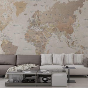 Puede incluir: Un salón moderno con un mural de mapa del mundo en tonos neutros. Un sofá gris y un sofá blanco con cojines a rayas están colocados frente al mapa. Una mesa de centro y mesas auxiliares completan la decoración.