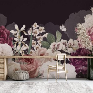 May include: Floral wallpaper featuring large, detailed illustrations of roses, irises, and other flowers in shades of burgundy, pink, and white against a dark background. A wooden desk, chair, and ottoman are in front of the wallpaper.