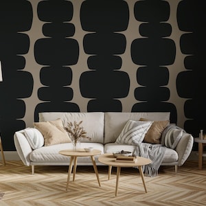 以下が含まれることがあります： ベージュのソファ、木製のコーヒーテーブル、フロアランプを備えたモダンなリビングルーム。壁には黒とベージュの幾何学模様があります。装飾的な枕とスローケットが空間に質感と色を追加します。