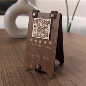 May include: A wooden sign with a QR code, five stars, and the text "Scan or Tap to review" and "Your Logo Here". The sign is on a wooden table.