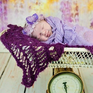 Peut inclure: Un b&eacute;b&eacute; endormi envelopp&eacute; dans une couverture lavande, portant un bandeau de fleurs violettes, est couch&eacute; dans un panier en osier blanc sur une balance vintage avec un cadran blanc et des chiffres noirs.