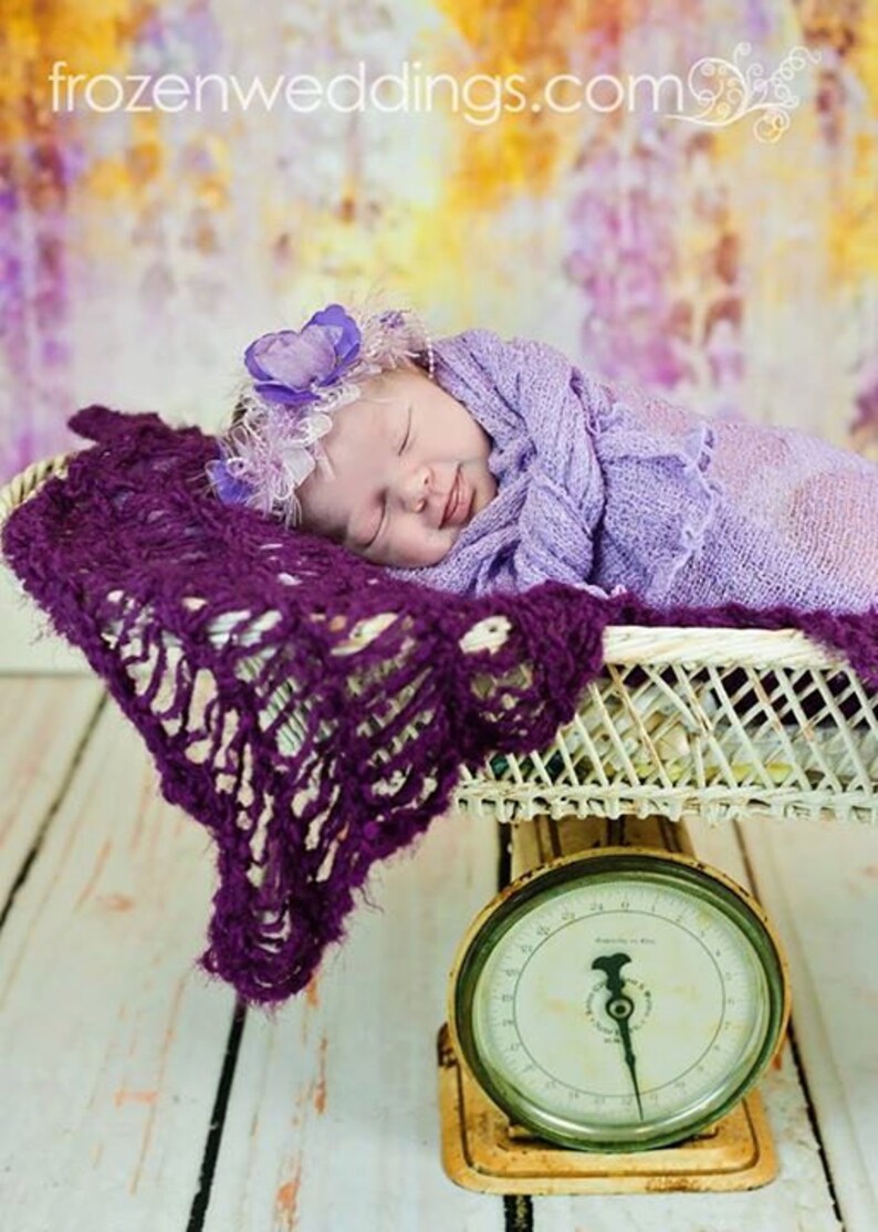 Peut inclure: Un b&eacute;b&eacute; endormi envelopp&eacute; dans une couverture lavande, portant un bandeau de fleurs violettes, est couch&eacute; dans un panier en osier blanc sur une balance vintage avec un cadran blanc et des chiffres noirs.