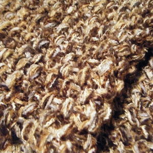 May include: Close-up of a brown and white fuzzy scarf made of yarn. The scarf is folded in half and the texture is visible.