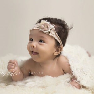 Peut inclure: Un b&eacute;b&eacute; portant un bandeau blanc avec une fleur, allong&eacute; sur une couverture blanche et moelleuse. Le b&eacute;b&eacute; sourit et regarde sur le c&ocirc;t&eacute;.