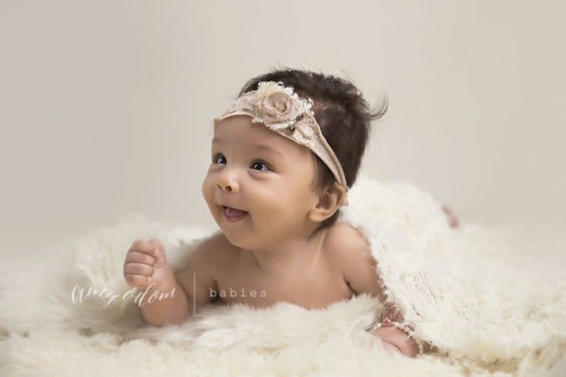 Peut inclure: Un b&eacute;b&eacute; portant un bandeau blanc avec une fleur, allong&eacute; sur une couverture blanche et moelleuse. Le b&eacute;b&eacute; sourit et regarde sur le c&ocirc;t&eacute;.
