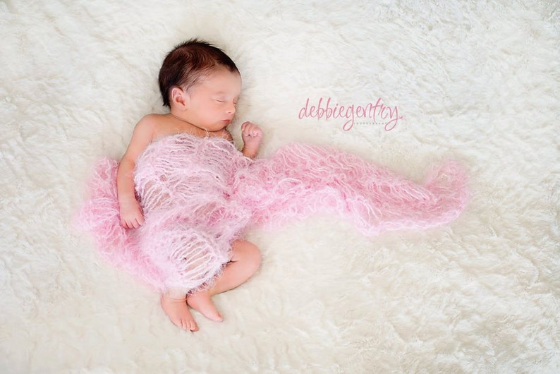 Peut inclure: Un nouveau-n&eacute; dort paisiblement envelopp&eacute; dans une couverture rose et moelleuse. Le b&eacute;b&eacute; est allong&eacute; sur une surface blanche et moelleuse. Le texte "debbie gentry photography" est visible dans le coin sup&eacute;rieur droit de l'image.