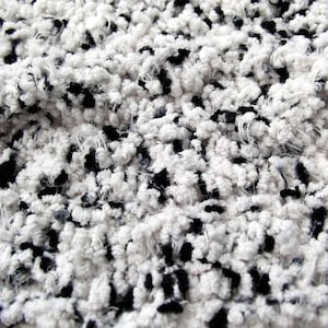 May include: Close-up of a white and black fuzzy fabric with a textured, fluffy surface.