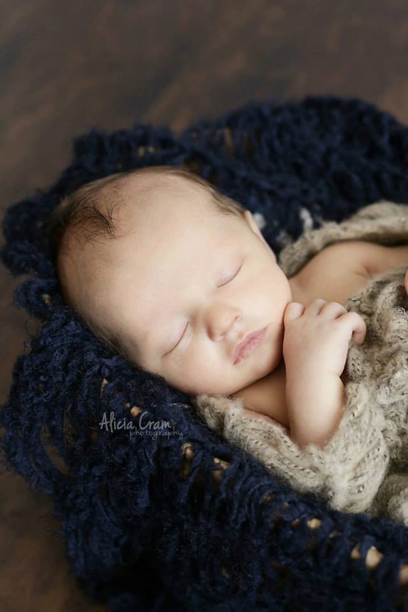 Peut inclure: Un nouveau-n&eacute; dort paisiblement dans une couverture en tricot bleu. Le b&eacute;b&eacute; porte un pull en tricot beige et a la main sous le menton.