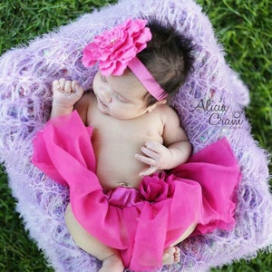 Peut inclure: Un b&eacute;b&eacute; fille portant un bandeau de fleurs rose et une jupe en tulle rose, allong&eacute; sur une couverture moelleuse violette. Le b&eacute;b&eacute; dort paisiblement.