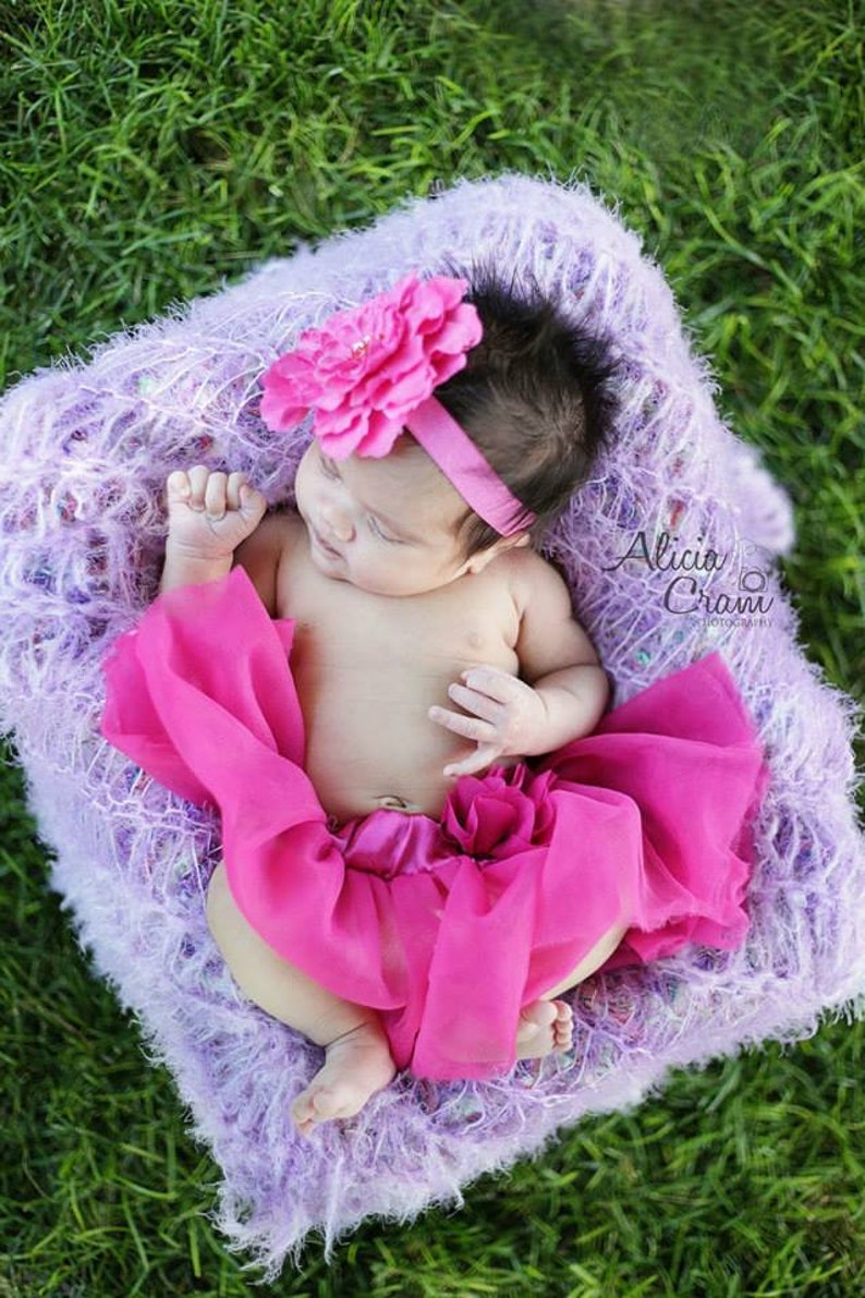 Peut inclure: Un b&eacute;b&eacute; fille portant un bandeau de fleurs rose et une jupe en tulle rose, allong&eacute; sur une couverture moelleuse violette. Le b&eacute;b&eacute; dort paisiblement.