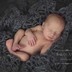 Peut inclure: Un nouveau-n&eacute; dort paisiblement sur une couverture moelleuse grise. Le b&eacute;b&eacute; est enroul&eacute; sur lui-m&ecirc;me, les bras et les jambes repli&eacute;s. Les yeux du b&eacute;b&eacute; sont ferm&eacute;s et son visage est d&eacute;tendu.