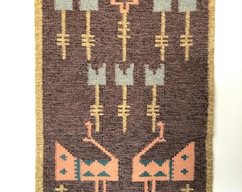 May include: A brown woven rug with a geometric design featuring stylized flowers and birds. The rug has a yellow border and is made with a variety of colors, including pink, blue, and gold.