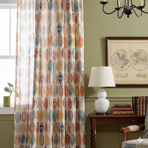 Puede incluir: Una cortina estampada con un diseño ovalado repetido en tonos de azul, naranja, amarillo y gris. La cortina cuelga frente a una ventana, con una lámpara y un mapa enmarcado en el fondo.