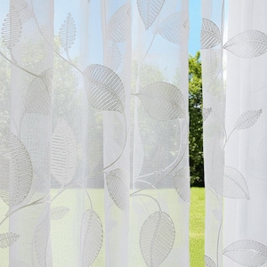 Puede incluir: Cortinas blancas transparentes con un delicado diseño de hojas. Las cortinas son semitransparentes, permitiendo que la luz se filtre. El diseño de hojas es de un color suave y neutro, creando un aspecto sutil y elegante. Las cortinas cuelgan frente a una ventana.