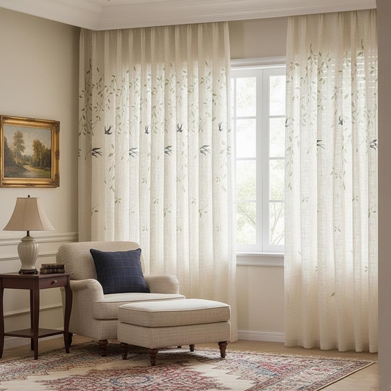 May include: Cream-coloured sheer curtains with a leaf and bird design. The curtains frame a window, and the room features a beige armchair, ottoman, and a small side table with a lamp. A framed landscape painting hangs on the wall.