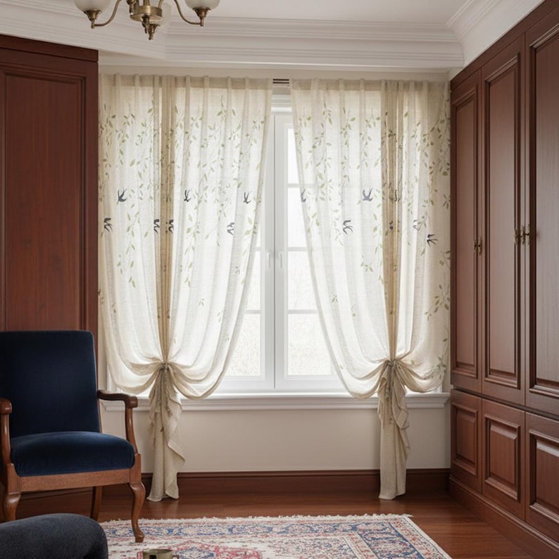 May include: Cream-coloured sheer curtains adorned with green leaves and bird motifs. The curtains are tied back, revealing a white window. The room includes dark wood furniture and a blue chair, creating a warm atmosphere.