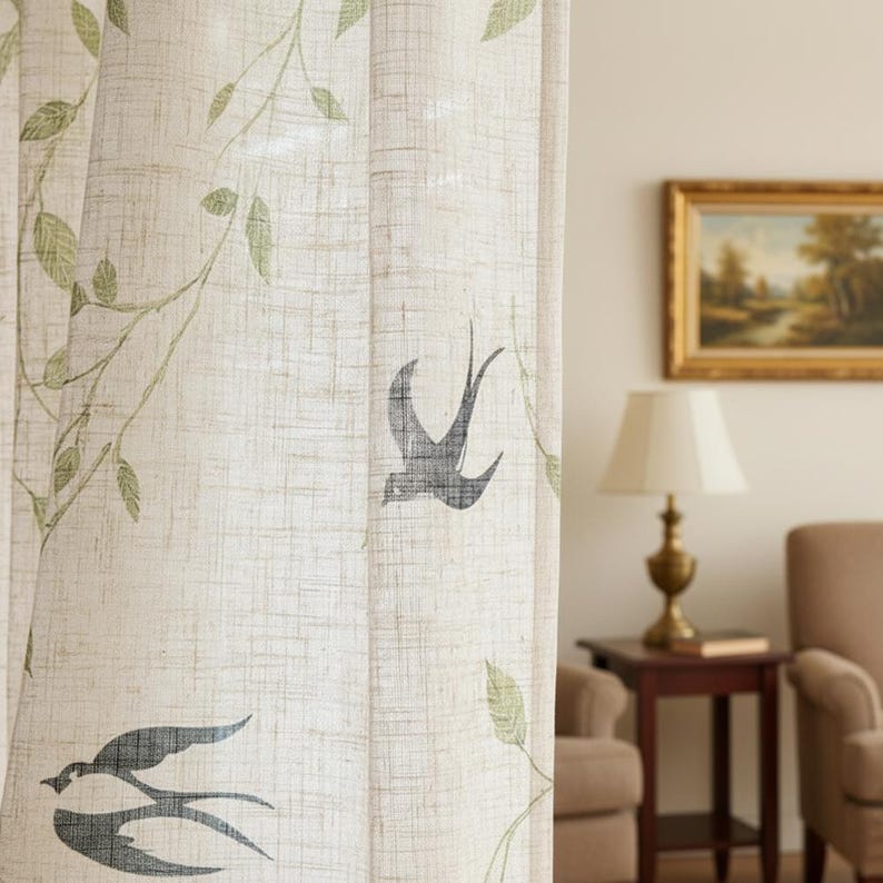 May include: Beige linen curtain with a nature-inspired design. The curtain features a repeating pattern of green leaves and stylized grey birds. The fabric has a textured appearance, and the design adds a touch of nature to the room.