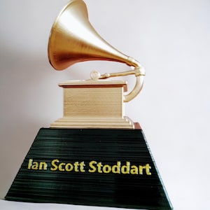 Könnte beinhalten: Eine goldfarbene Grammy-Trophäe mit dem Namen "Ian Scott Stoddart" auf dem Sockel.