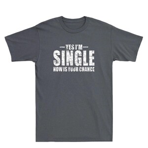 May include: Dark gray t-shirt with the text "YES I'M SINGLE NOW IS YOUR CHANCE" in distressed white lettering. The shirt is a crew neck style and appears to be made of a soft cotton blend.