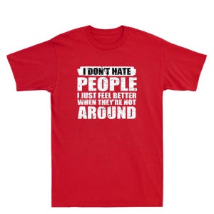 May include: Red t-shirt with white text that reads "I DON'T HATE PEOPLE I JUST FEEL BETTER WHEN THEY'RE NOT AROUND." The text is in a bold, sans-serif font. The shirt is a crew neck style.