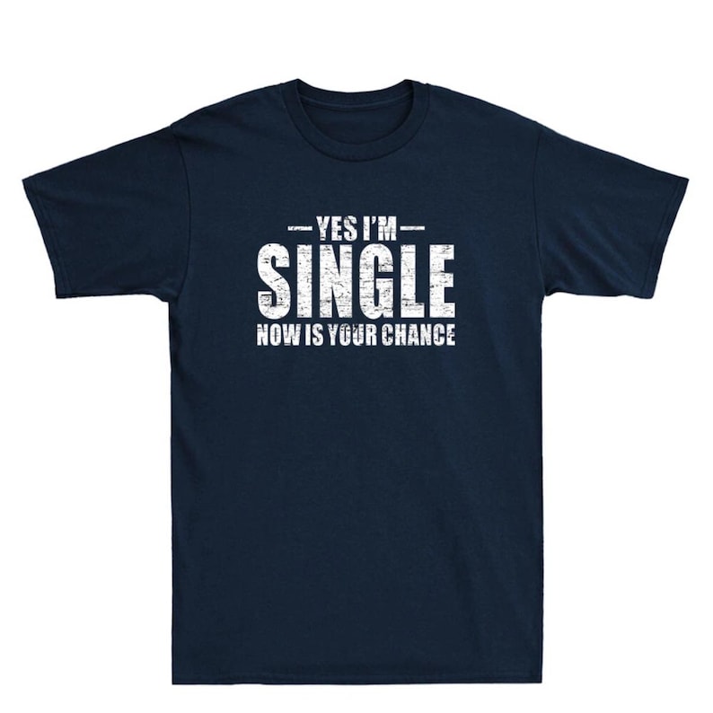 May include: Navy blue t-shirt with the white text "YES I'M SINGLE NOW IS YOUR CHANCE". The text has a distressed, vintage look. The shirt is a short-sleeved crew neck.