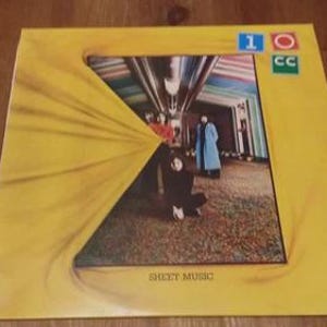 Puede incluir: Portada de álbum de vinilo vintage para "Sheet Music" de 10cc. La portada es amarilla con una imagen central de una habitación con personas. El nombre de la banda está en un cuadro azul y verde en la esquina superior derecha.