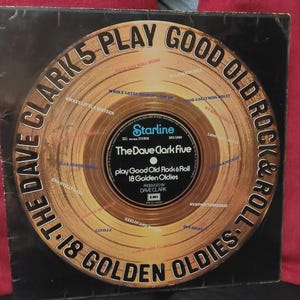 Könnte beinhalten: Vintage Vinyl-Schallplattenhülle für "The Dave Clark Five Play Good Old Rock & Roll: 18 Golden Oldies". Das Albumcover zeigt ein goldfarbenes Plattendesign mit dem Bandnamen und dem Albumtitel in fetter Schrift. Die Schallplatte befindet sich auf schwarzem Hintergrund.