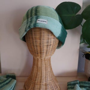 May include: A green and blue tie-dye beanie hat with a small white tag that reads "RE-WIRED". The hat is displayed on a wicker mannequin head. Matching green and blue socks are visible in the foreground.