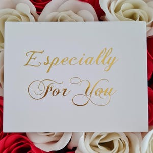 May include: A white card with gold lettering that reads "Especially For You" is surrounded by red and cream-colored roses. The card is centered in the image, with the roses forming a colorful backdrop.