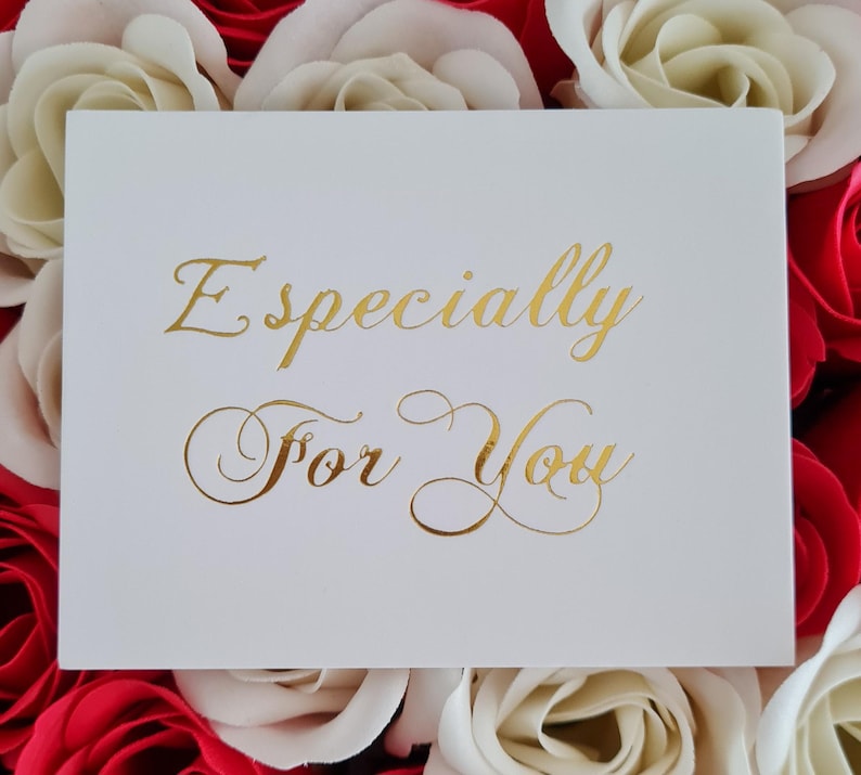 May include: A white card with gold lettering that reads "Especially For You" is surrounded by red and cream-colored roses. The card is centered in the image, with the roses forming a colorful backdrop.